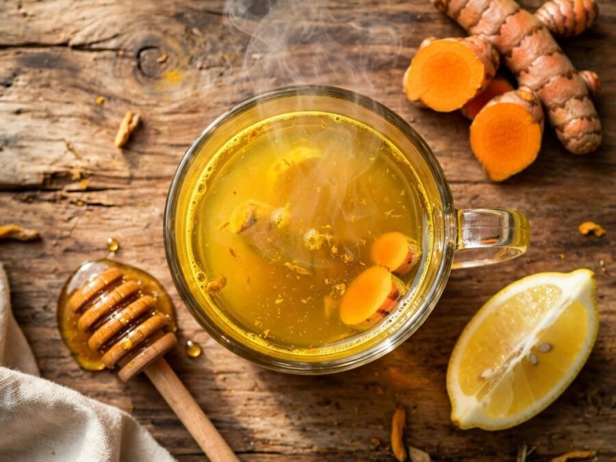 Glass mug of golden turmeric tea with fresh turmeric slices, lemon wedge and honey dipper