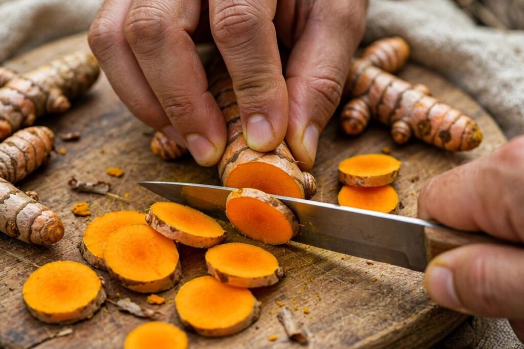 Hands slicing fresh turmeric root into thin rounds on a wooden cutting board