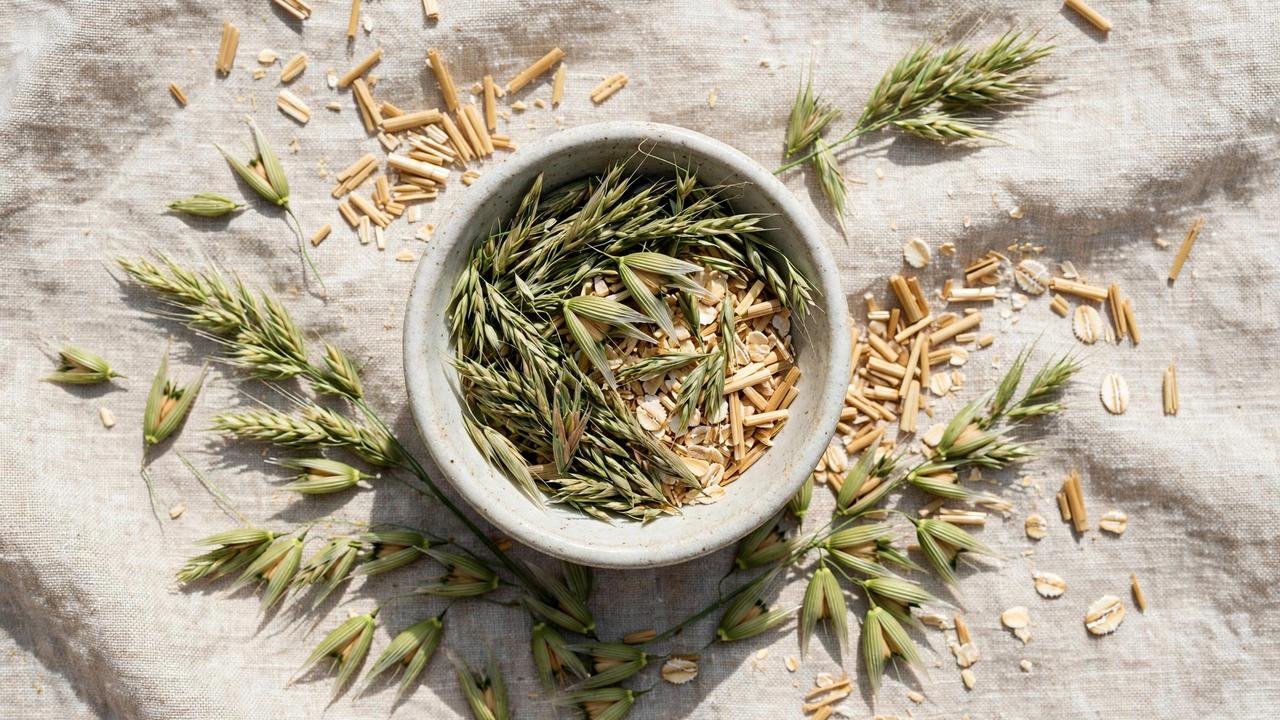 Top-down view of dried green oat tops and chopped oat straw in a ceramic bowl on a linen cloth