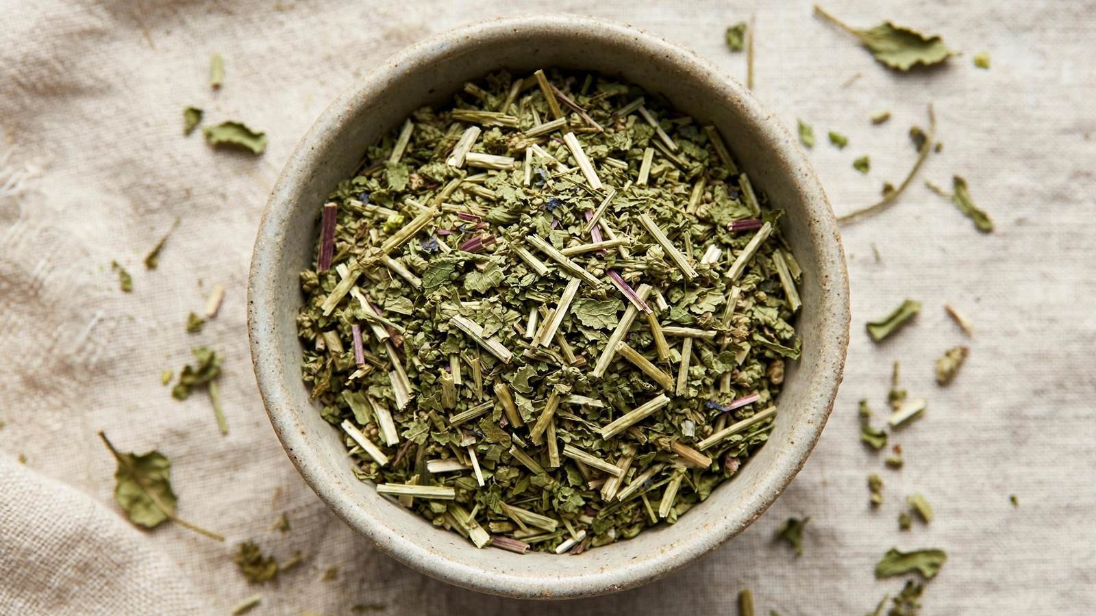 Top-down view of dried skullcap herb leaves in a small ceramic bowl on a linen cloth