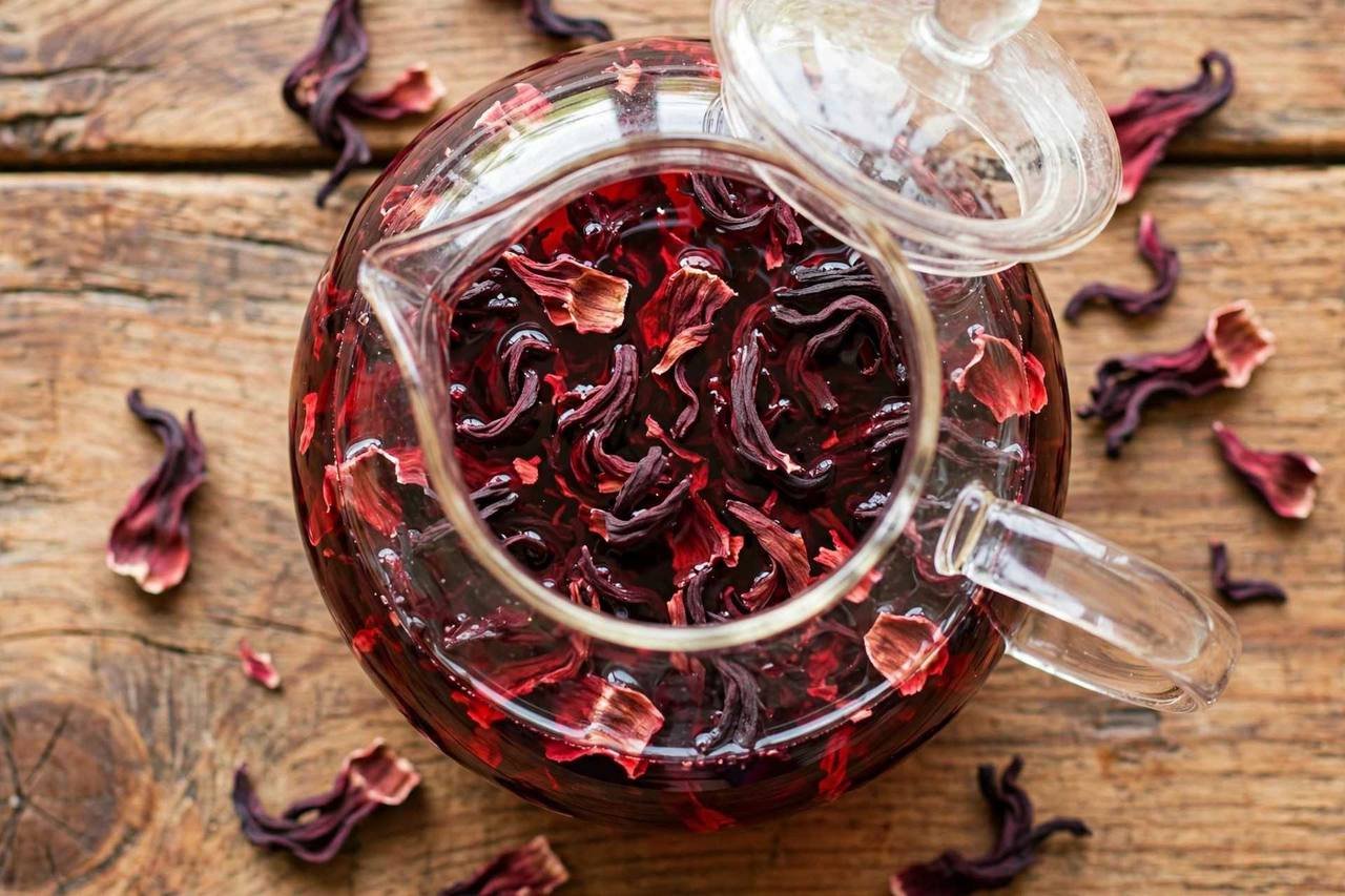 Dried hibiscus petals steeping in a glass teapot, water turning deep red